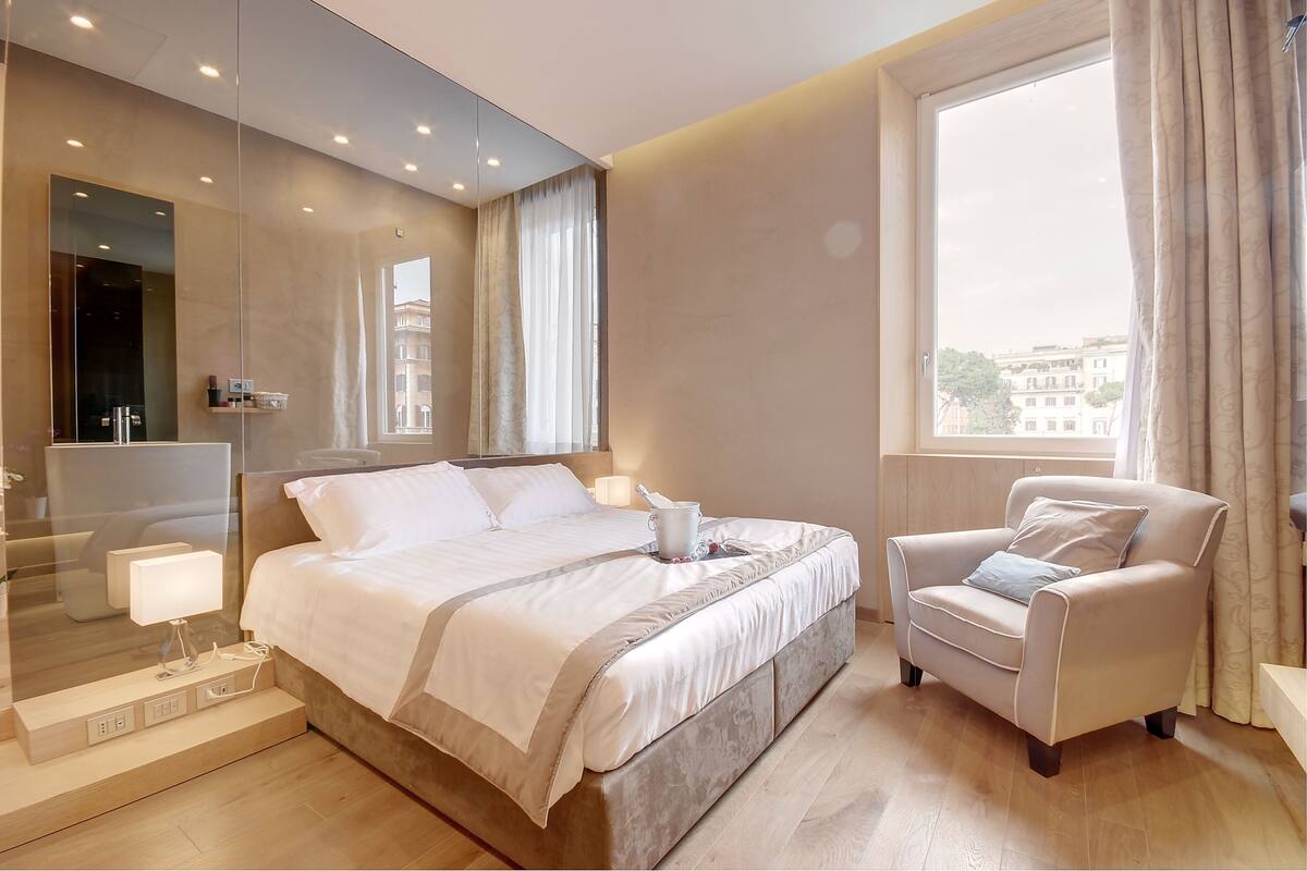 A modern hotel room with a large bed, a sitting area, and a view of the city.
