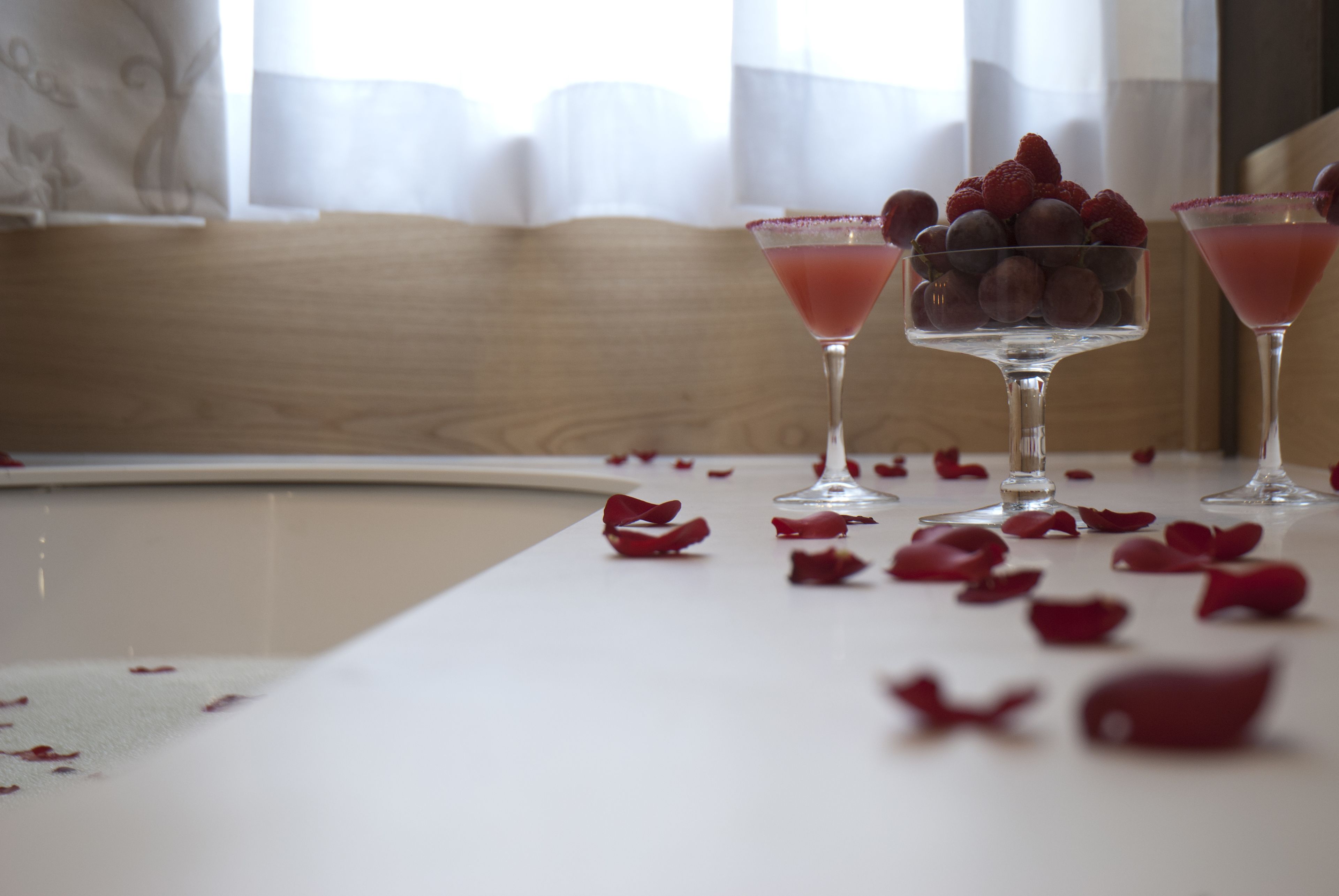 A table with two martini glasses, each containing a pink drink and a bowl of strawberries.