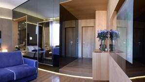 Una habitación de hotel moderna con una cama grande, un sofá azul, un separador de vidrio y un mostrador de recepción de madera.
