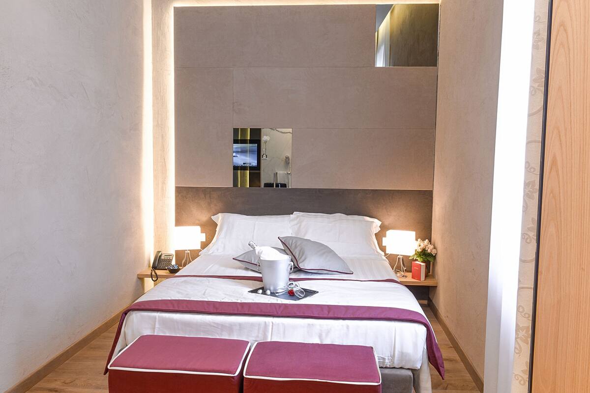 A hotel room with a large bed, bedside tables, a TV, and a mirror.