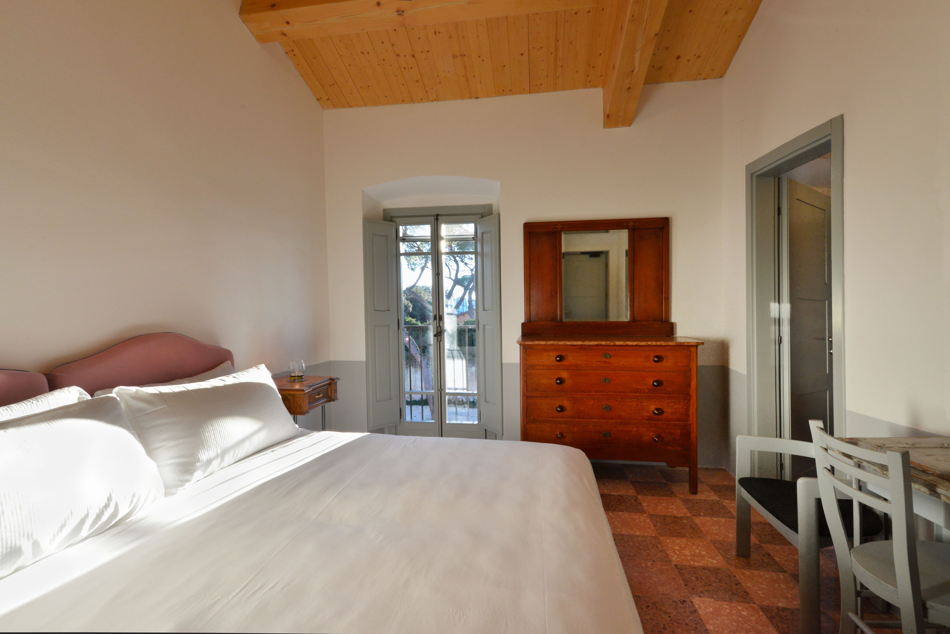 A bedroom with a bed, dresser, chair, and a door leading to a balcony.