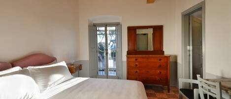 A bedroom with a bed, dresser, chair, and a door leading to a balcony.