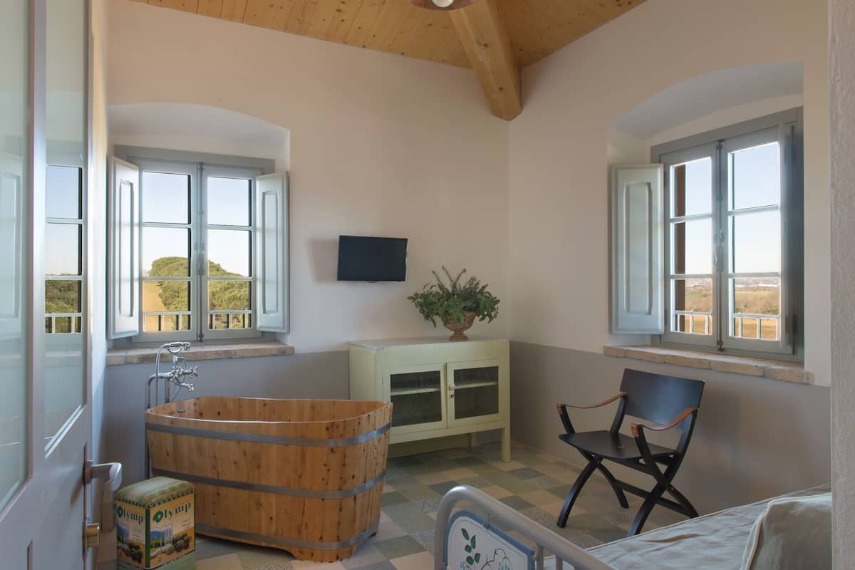 A bathroom with a wooden bathtub, a chair, and a cabinet with a plant.