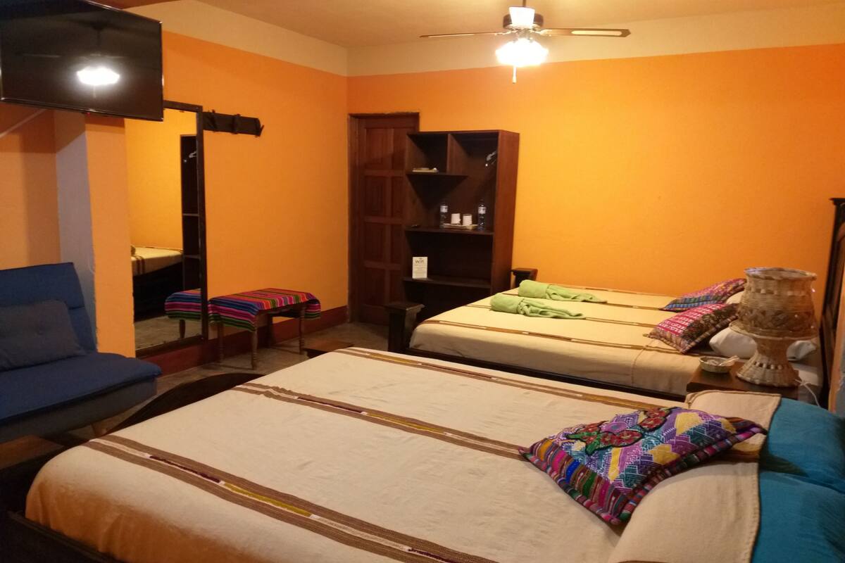 Une chambre d’hôtel avec deux lits, un canapé, une télévision et un ventilateur de plafond.