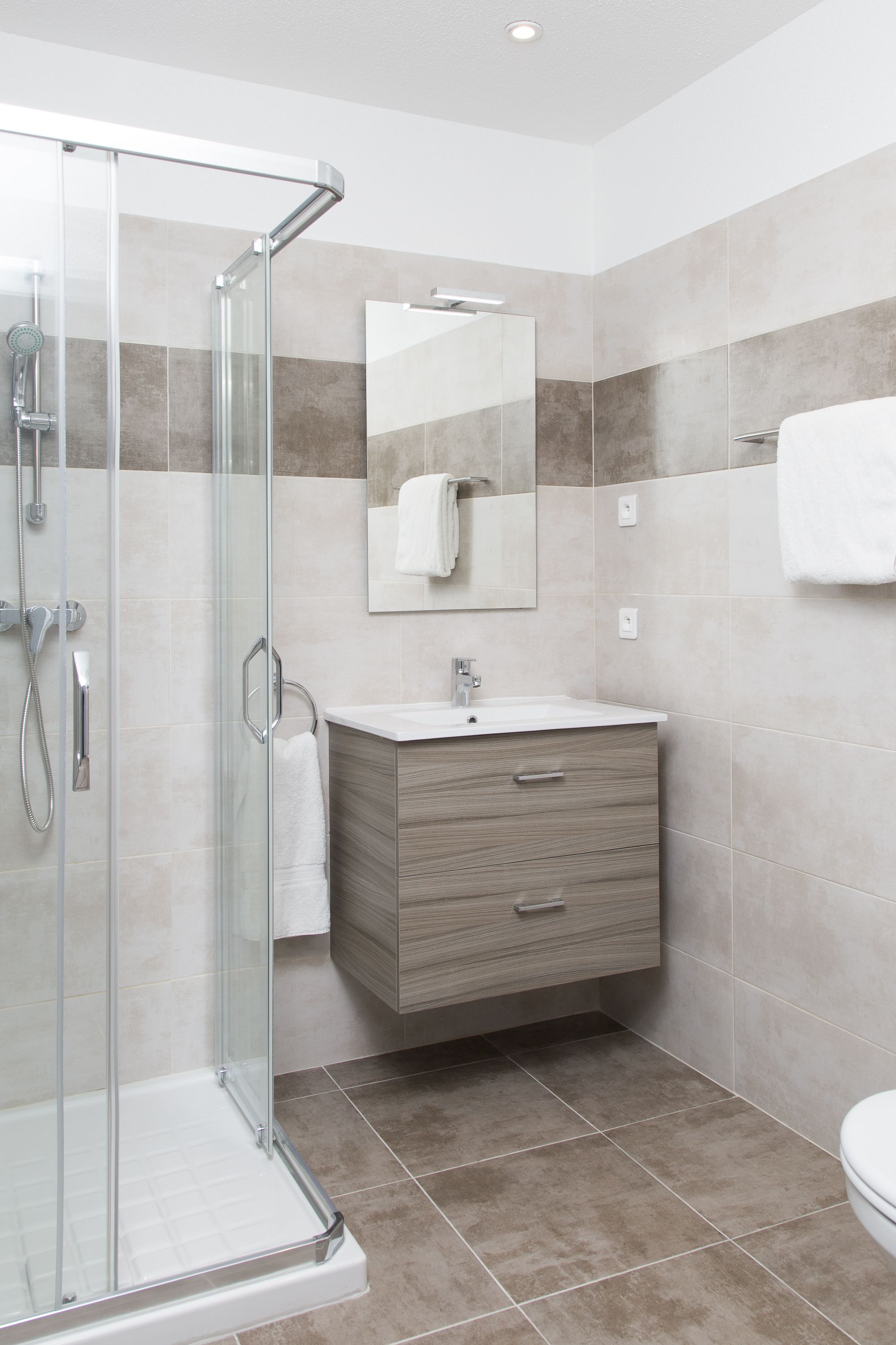 A modern bathroom with a glass shower enclosure, a wooden vanity, and a large mirror above the sink.