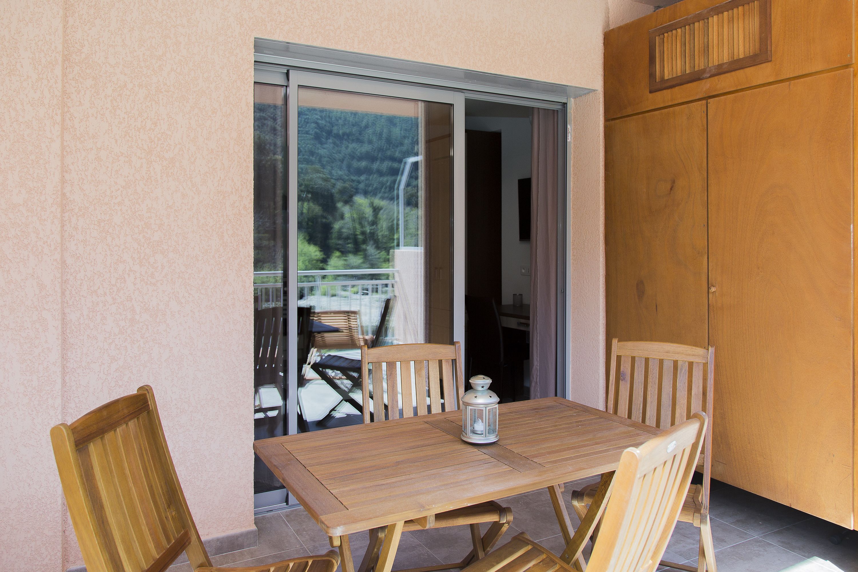 Una mesa de madera con cuatro sillas y un farol en un balcón con puerta corrediza de vidrio.