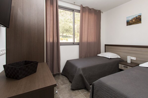 Habitación de hotel con dos camas, un escritorio, una ventana con cortinas, un cuadro en la pared y un cubo de basura.