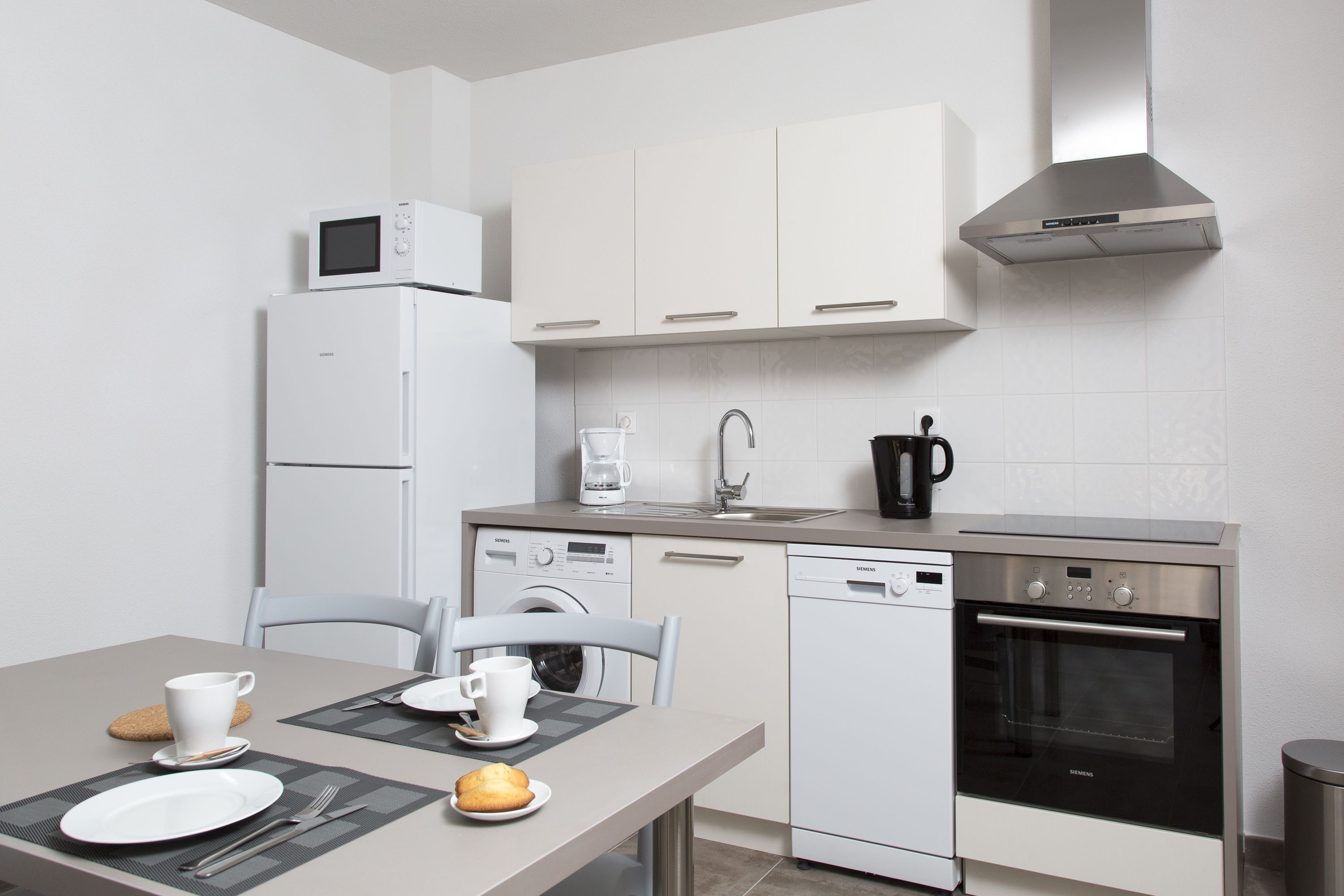 Een moderne keuken met witte kasten, een magnetron, een koffiezetapparaat, een vaatwasser en een oven.