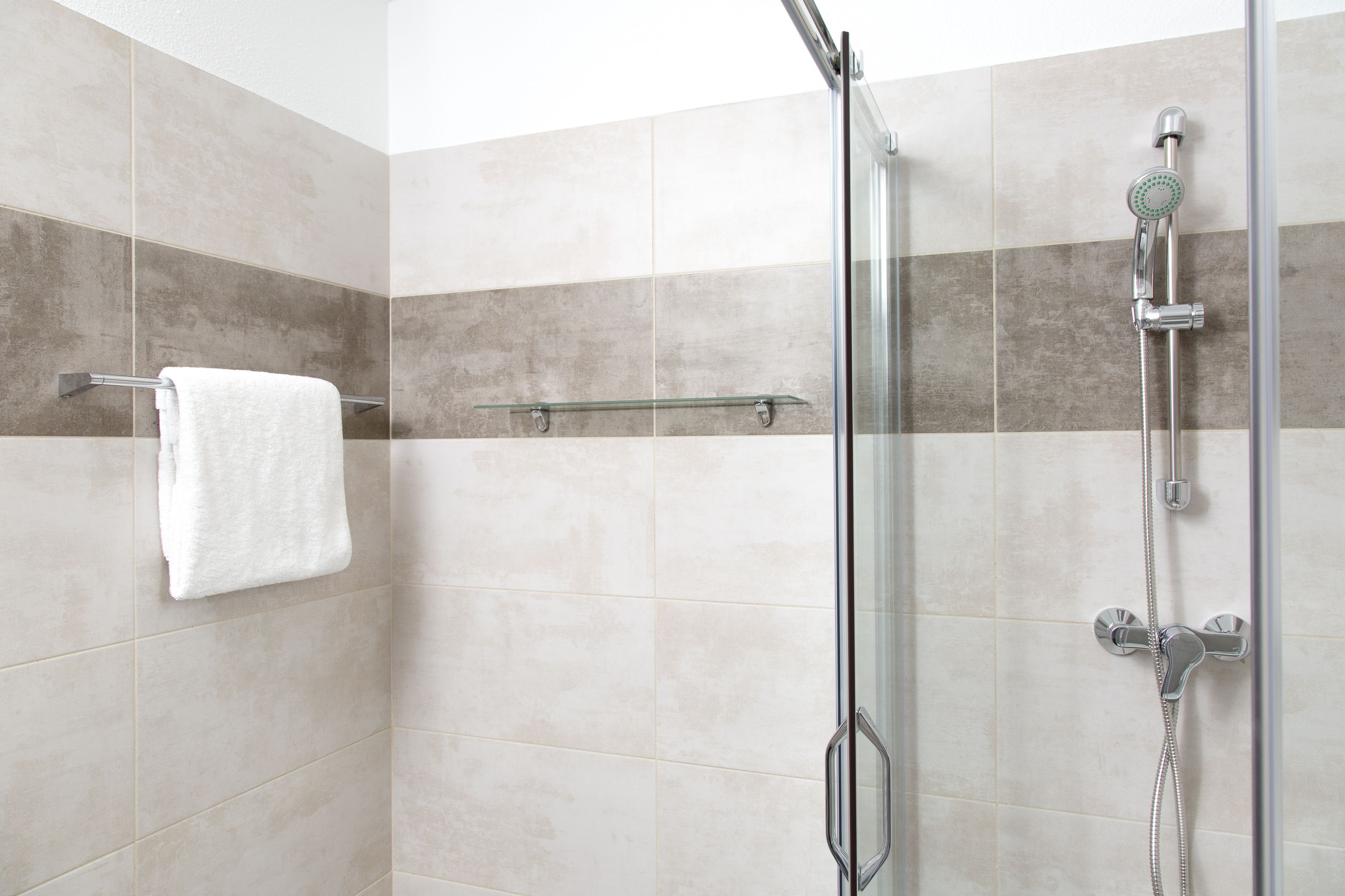 A modern shower area with a glass door, a white towel hanging on a rack, and a showerhead with multiple nozzles.