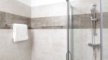 A modern shower area with a glass door, a white towel hanging on a rack, and a showerhead with multiple nozzles.