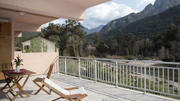 A balcony with a view of mountains, a table with chairs, and a potted plant.