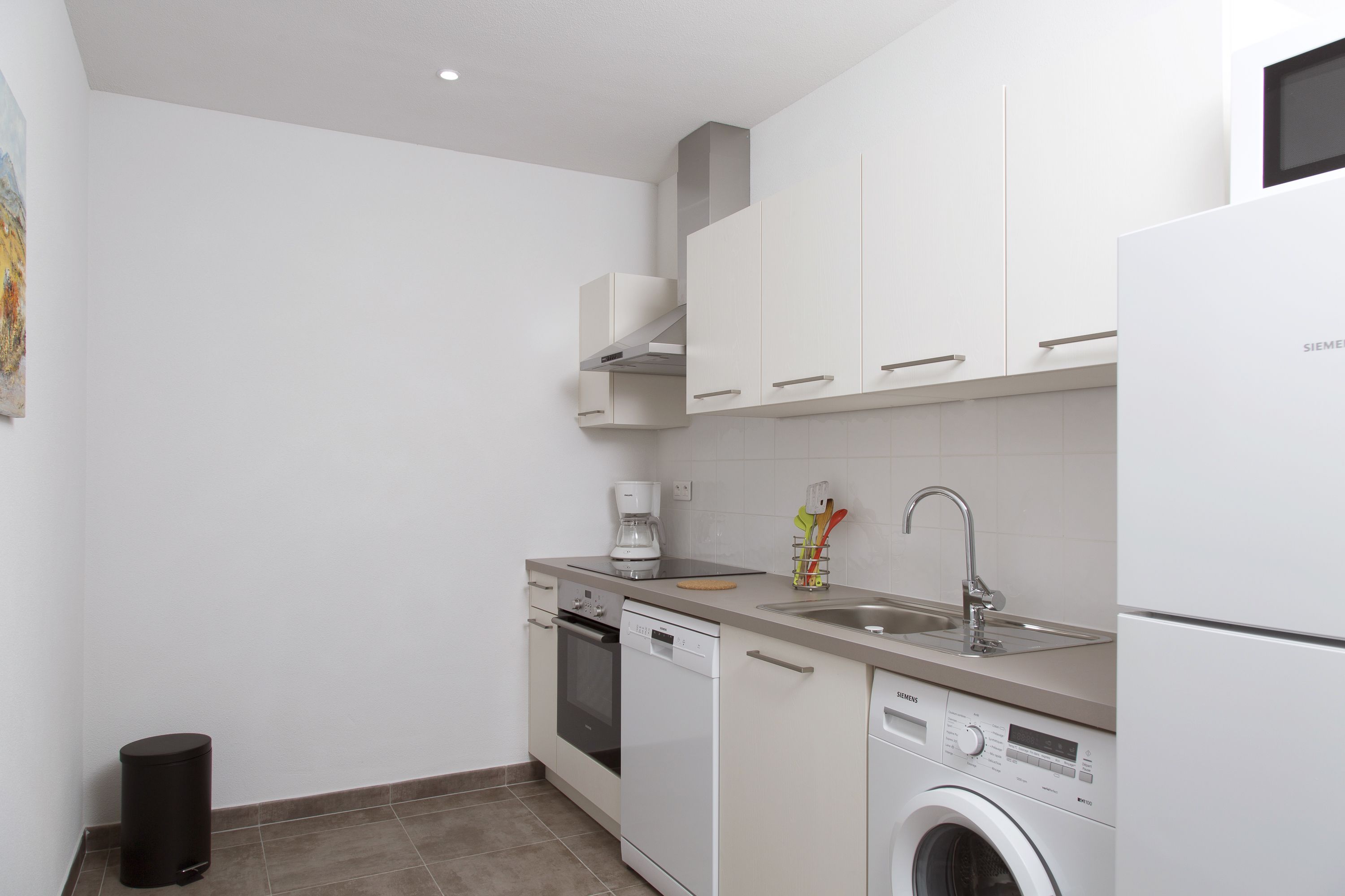 A compact kitchen with white cabinets, a coffee maker, a dishwasher, and a washing machine.