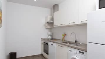 A compact kitchen with white cabinets, a coffee maker, a dishwasher, and a washing machine.