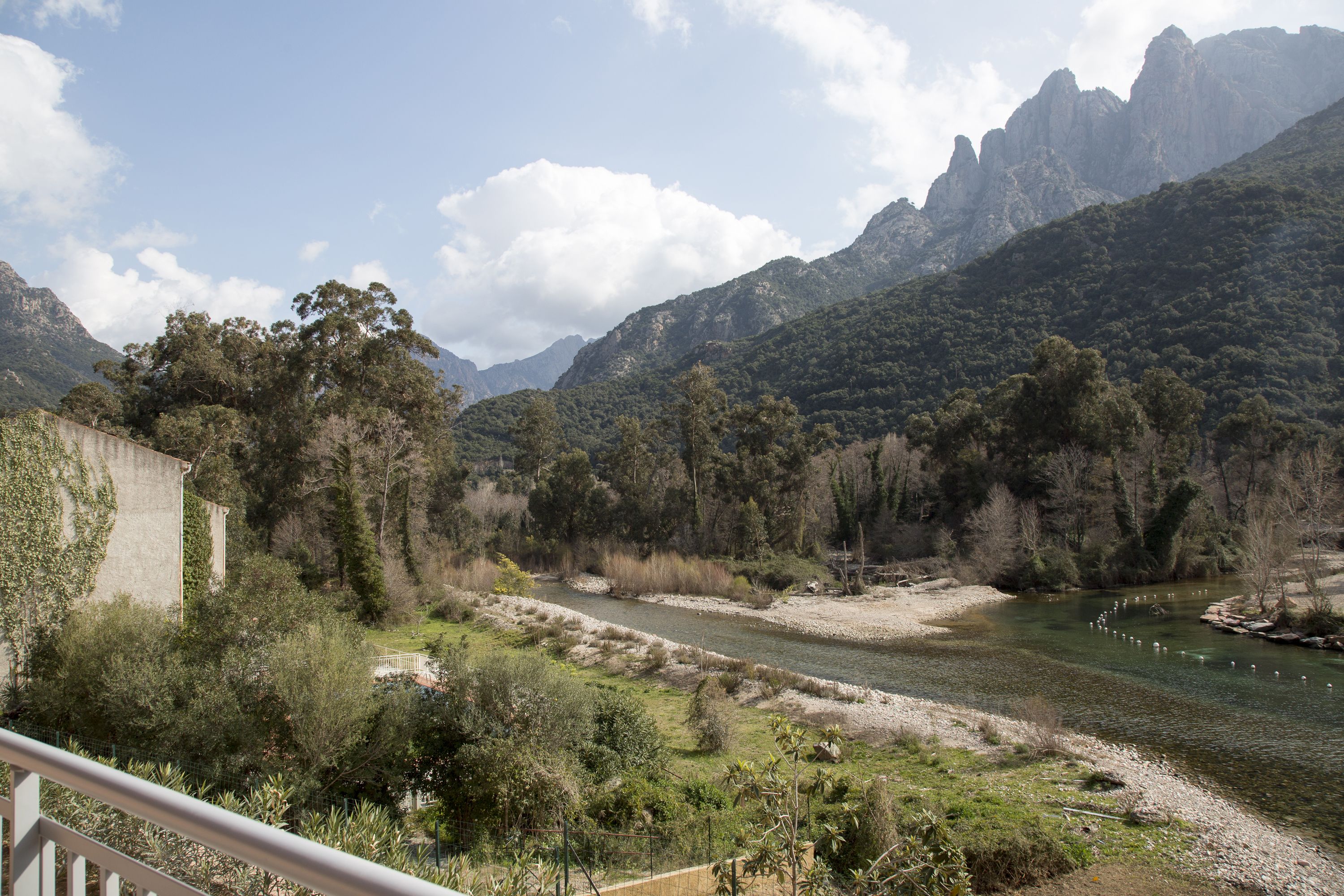 A river flowing through a mountainous landscape with dense vegetation and a building on the left.