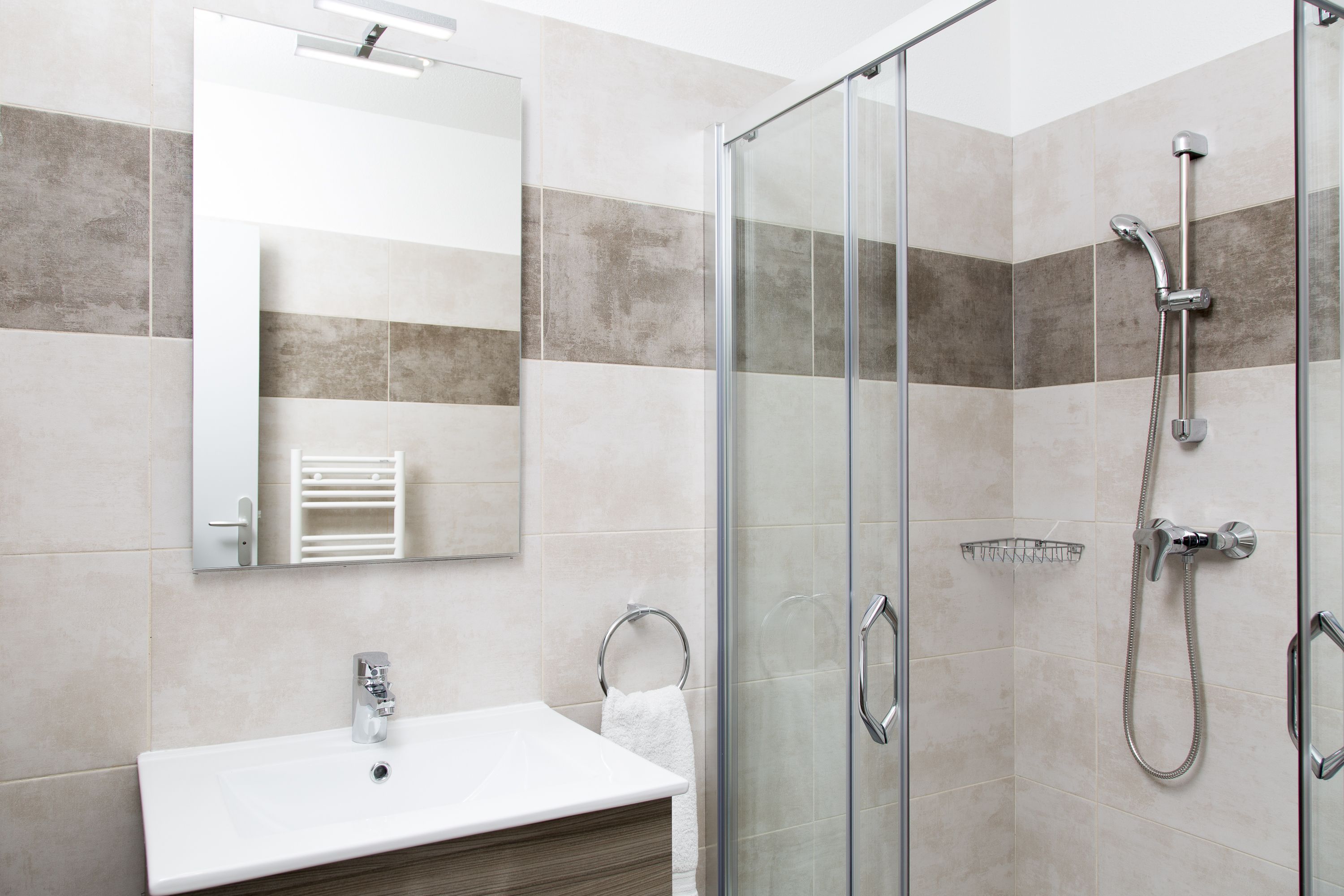 Een moderne badkamer met een douchecabine van glas, een wit wastafelmeubel en een spiegel.