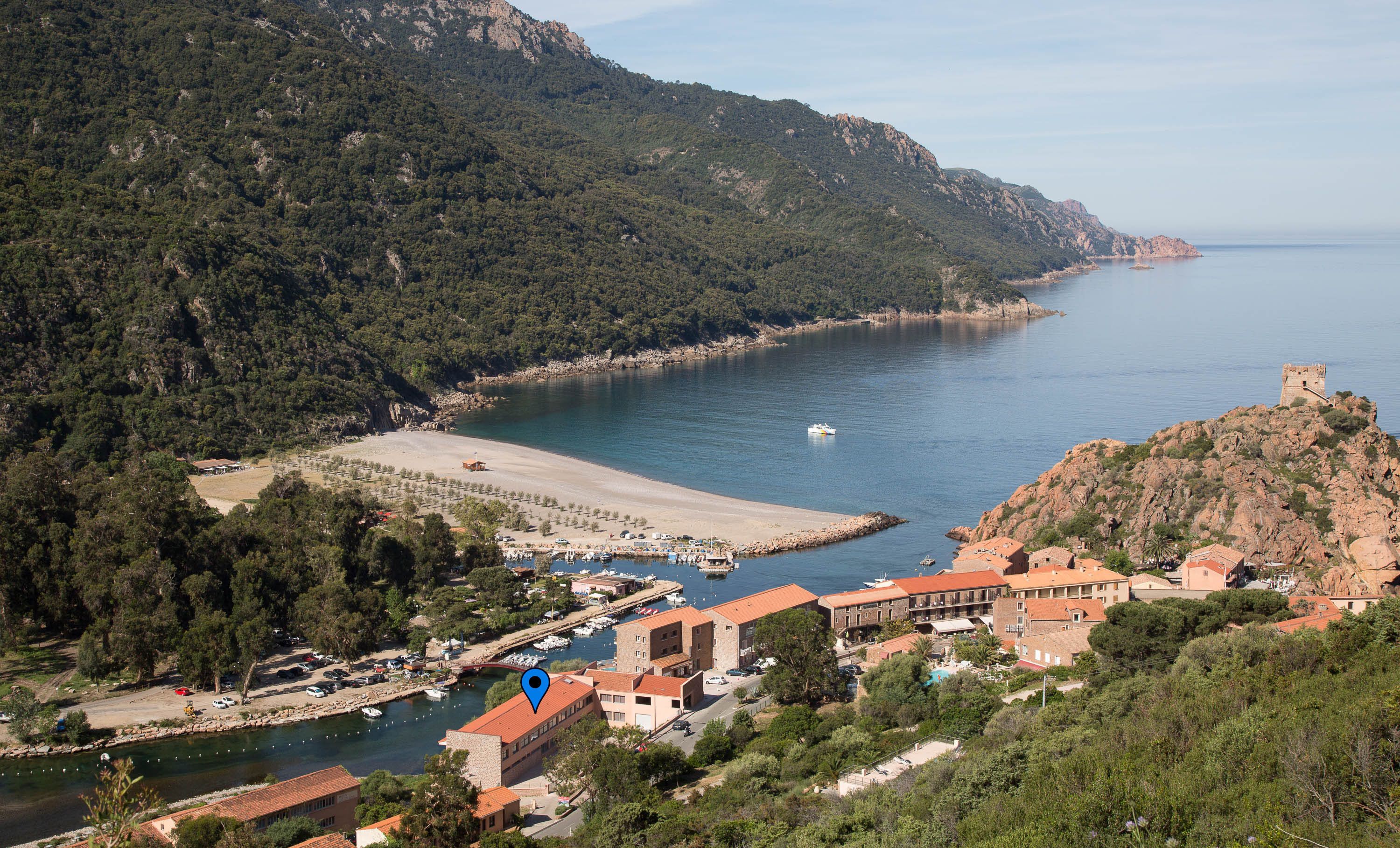 Une ville côtière dotée d’un port de plaisance, d’une plage de sable et d’une structure ressemblant à un château, située sur une colline.