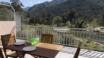 Un balcón con una mesa dispuesta para dos, con vista a un río y montañas.