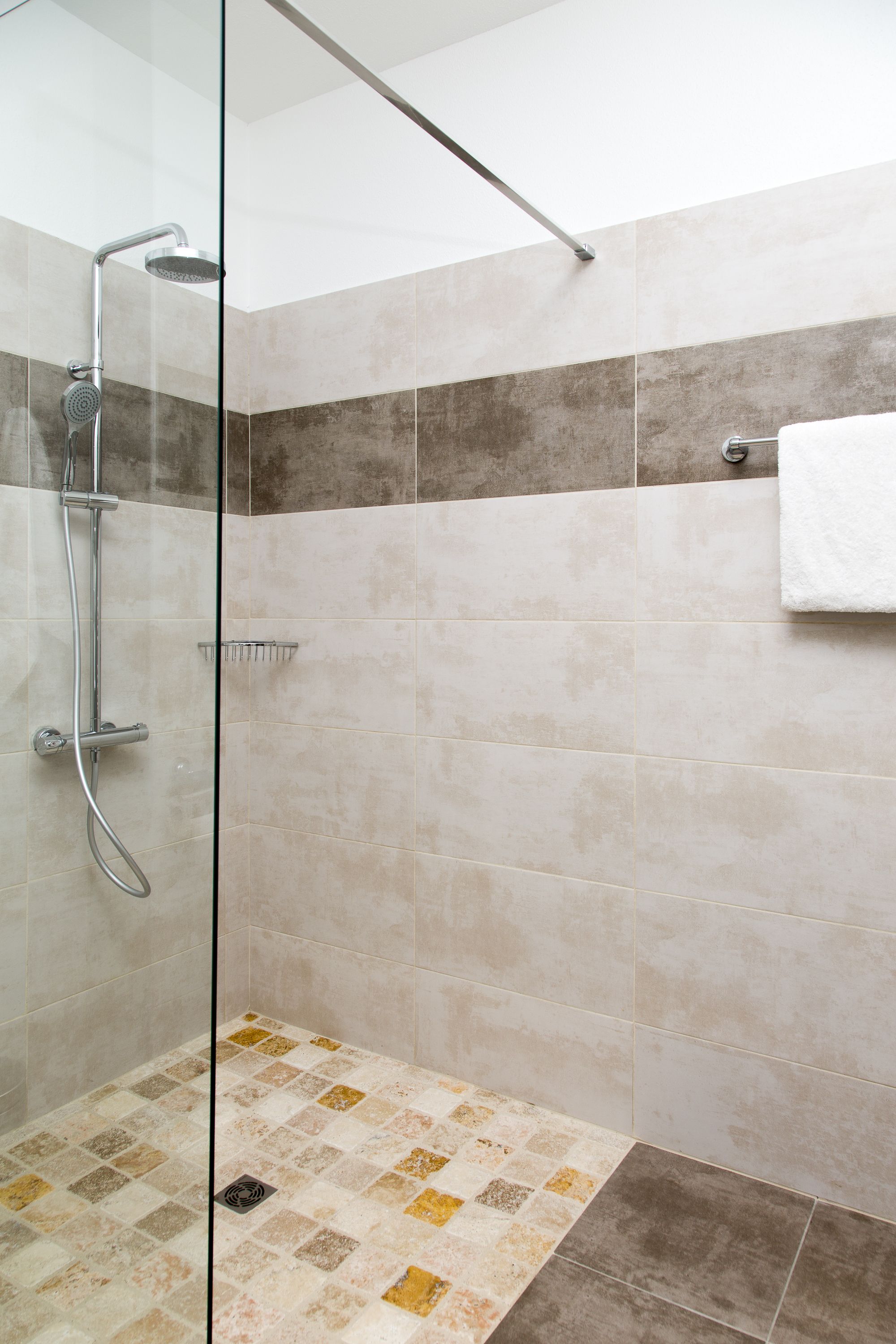Ein modernes Duschbad mit Glastrennwand, Handbrause und Handtuchhalter.
