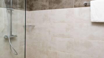Een moderne douchecel met glazen wand, handdouche en handdoekhouder.