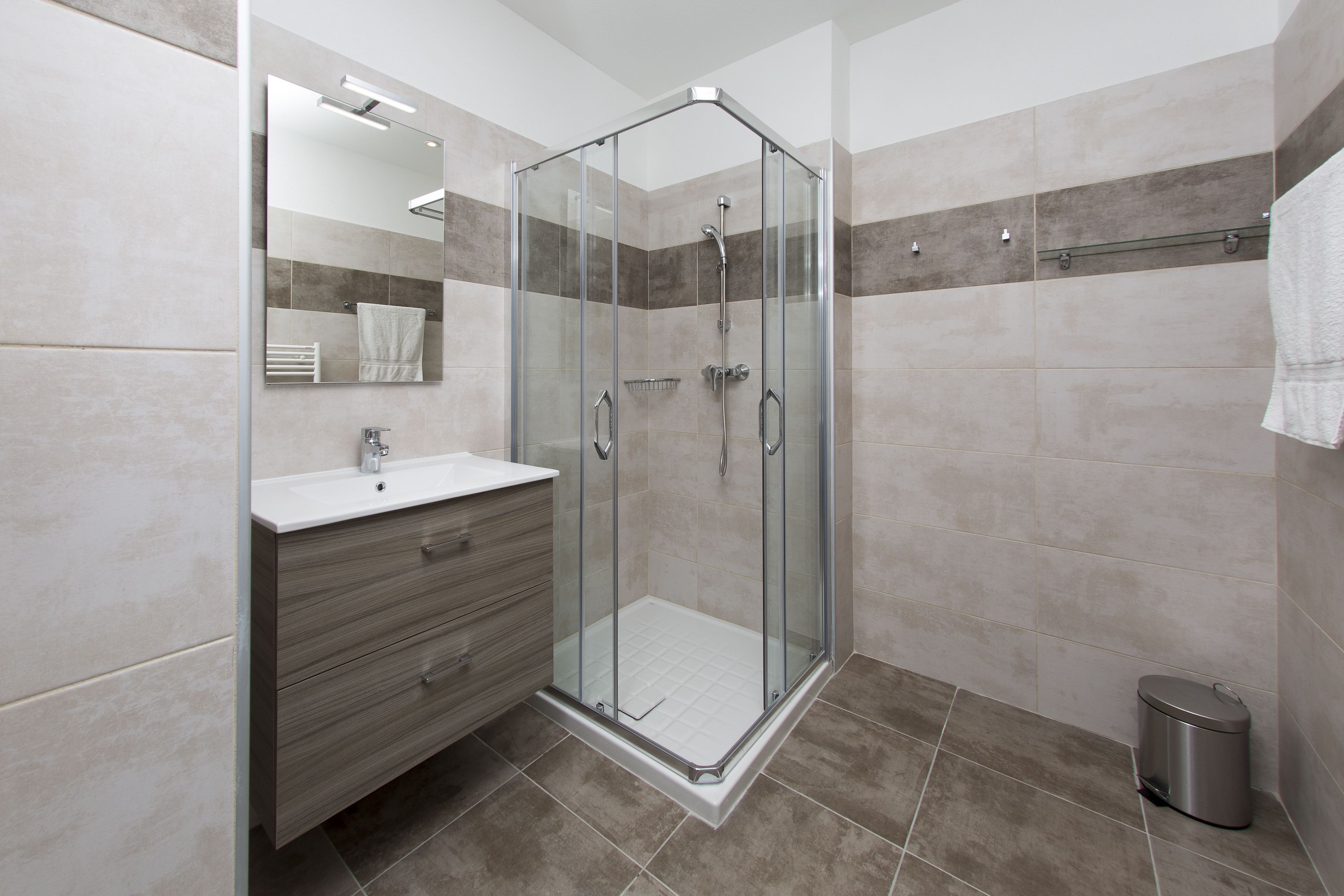 A modern bathroom with a glass-enclosed shower, a vanity with a mirror, and a trash bin.
