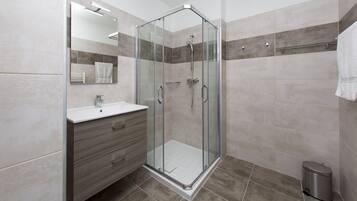 A modern bathroom with a glass-enclosed shower, a vanity with a mirror, and a trash bin.