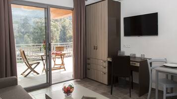 A modern room with a sliding glass door leading to a balcony, a flat-screen TV mounted on the wall, a dining table with chairs, and a sofa.