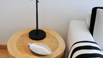 A round wooden table with a black lamp, a white cushion, and a striped throw blanket on a white sofa.