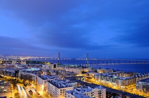 A cityscape at dusk with a prominent bridge in the background and a view of the waterfront. - Panoramic Living (Lisbon)