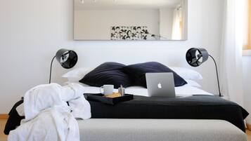 Una cama bien hecha con un ordenador portátil, una bandeja con una taza y un pastel, y una obra de arte blanco y negro en la pared.