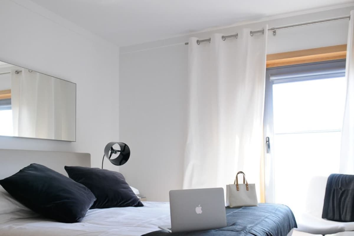 A modern hotel room with a bed, a laptop, a handbag, and a chair.