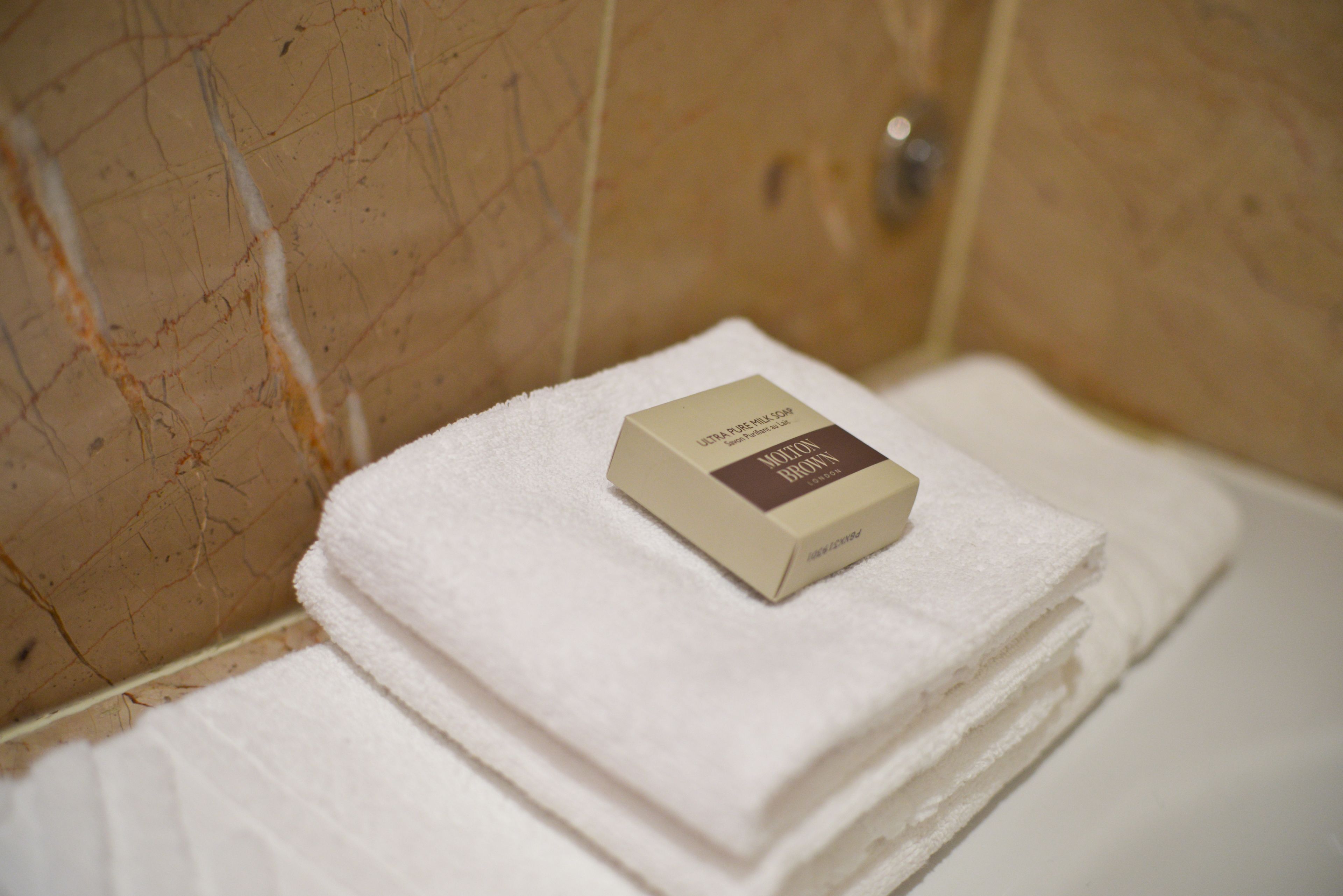 Un baño con pared de mármol, una toalla blanca y una pastilla de jabón.