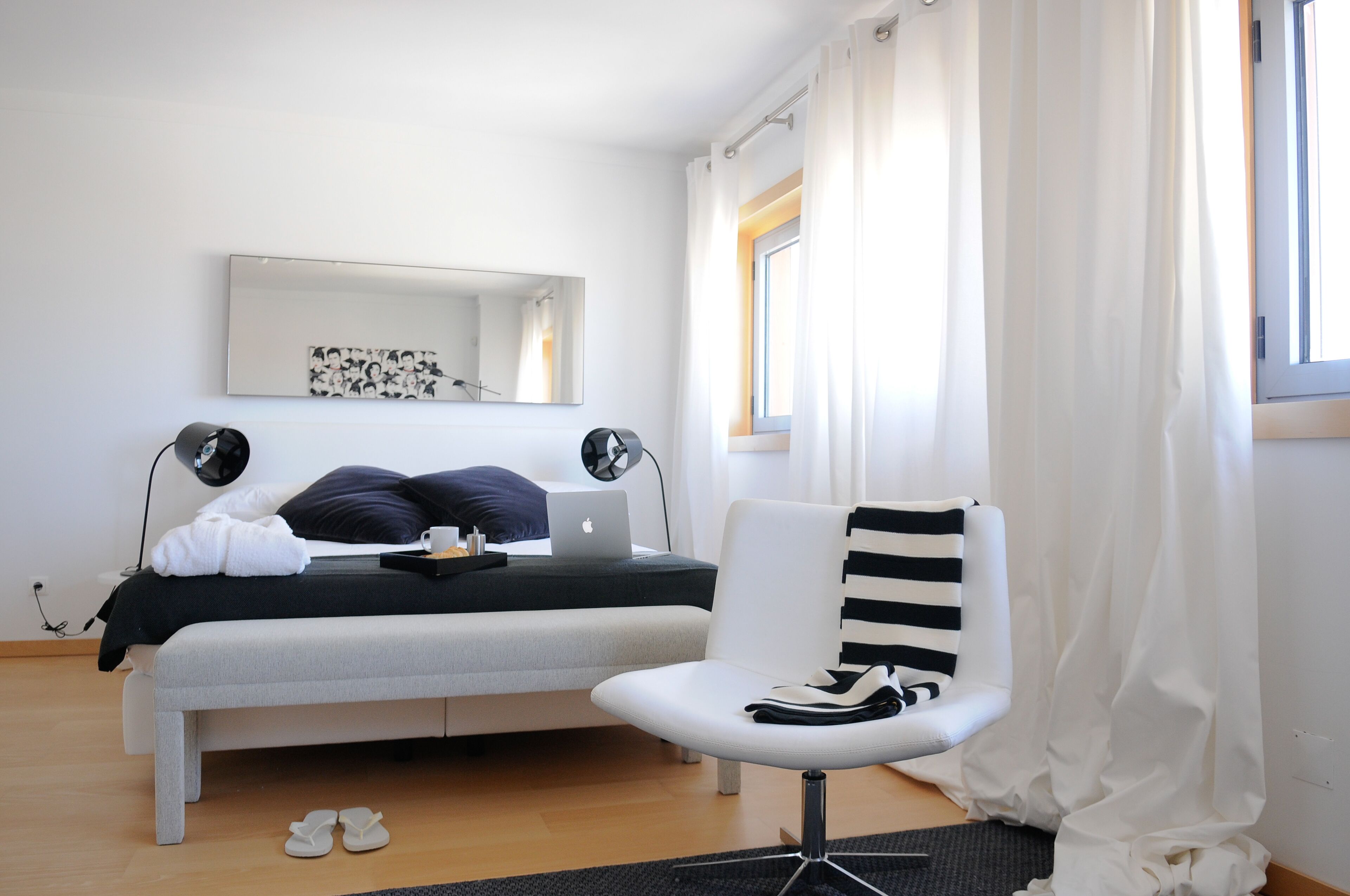 A modern bedroom with a bed, a laptop, a chair, and a window with curtains.