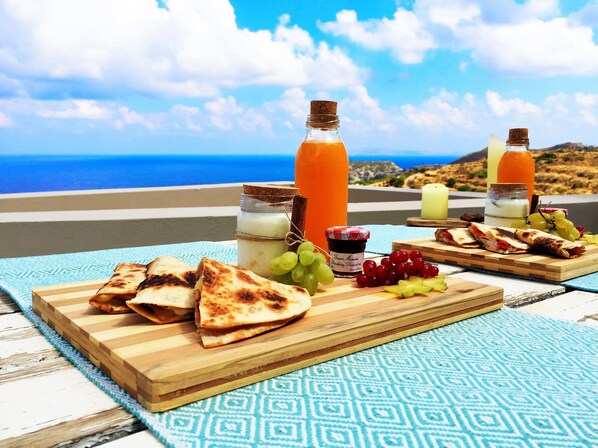Una mesa con comida y bebidas en una terraza con vistas al mar.