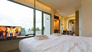 Une chambre d’hôtel moderne dotée d’un grand lit, d’une télévision et offrant une vue sur l’extérieur grâce à de grandes fenêtres.