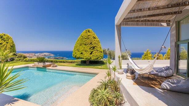 Un espace piscine extérieur moderne avec vue sur la mer, un hamac et un coin salon agrémenté de coussins.