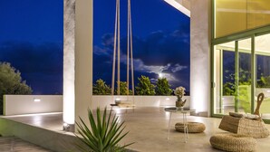 Un espace extérieur aménagé en terrasse, doté d’un design moderne, comprenant un coin salon et offrant une vue sur le ciel nocturne.