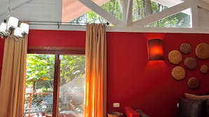 A room with a red wall, a large window with curtains, a sofa, and a wall-mounted light fixture.