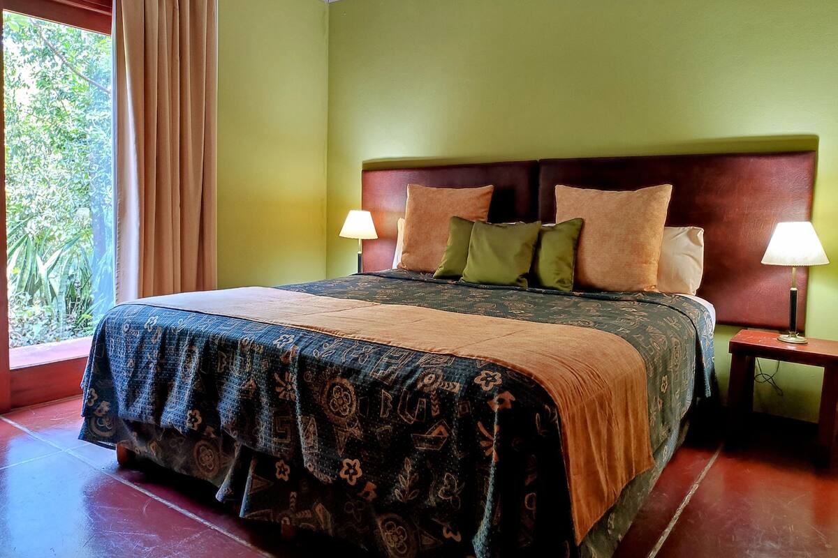 A bed with a patterned bedspread, two bedside lamps, and a headboard with multiple pillows.
