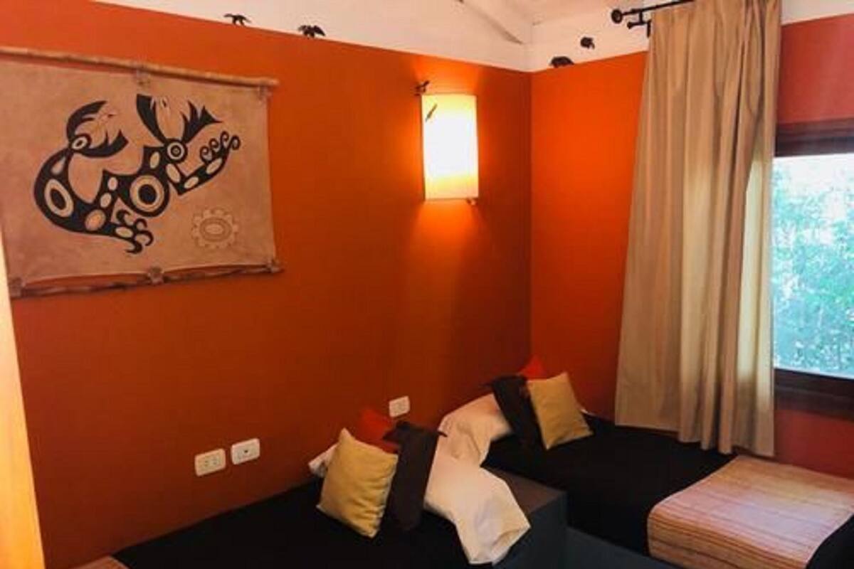 A room with two beds, a wall-mounted light, and a window with curtains.