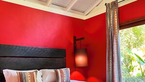 A bedroom with a large bed, red walls, a wooden headboard, and a window with curtains.