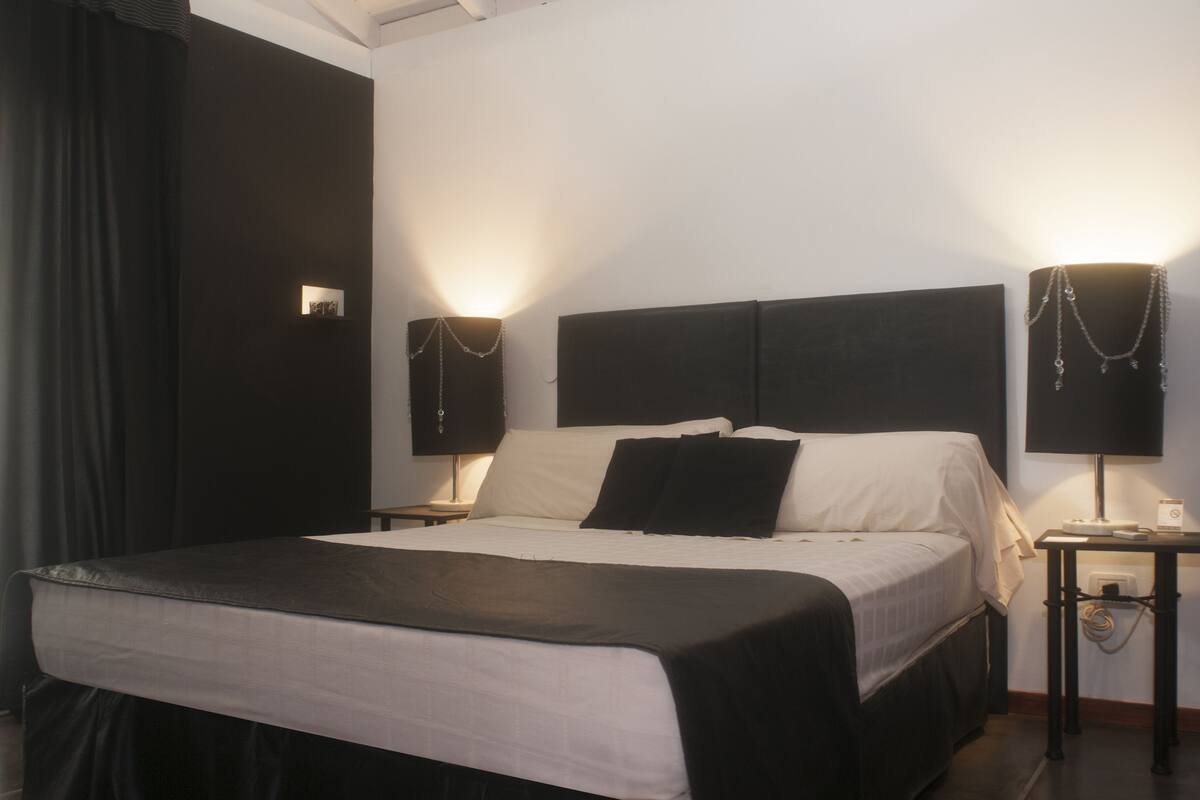 A hotel room with a bed, two bedside tables, a lamp, and a wall-mounted light fixture.
