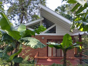 A house with a sloped roof, brick walls, and large green leaves in the foreground. - Raices Amambai Lodges (Puerto Iguazú)