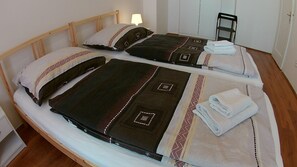 Ein Doppelbett mit zwei Kissen und einer Decke, ein gefaltetes Handtuch und ein Stuhl in einem Zimmer mit Holzboden und weißer Wand.