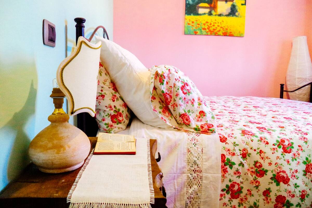 Ein Schlafzimmer mit einem Bett, einem Nachttisch mit Lampe, einem Buch und einem Wandbild.