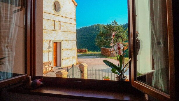 Une vue depuis une fenêtre d’un bâtiment, avec une petite porte et une fenêtre, un banc à l’extérieur et une plante à l’intérieur.