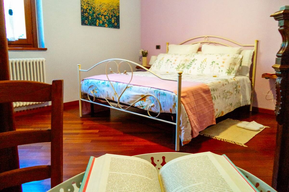 Ein Schlafzimmer mit einem Metallbettgestell, einem Holzstuhl, einem Heizkörper und einem Gemälde an der Wand.