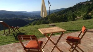 Une terrasse avec une table et deux chaises, donnant sur une vallée avec des collines et un ciel dégagé.
