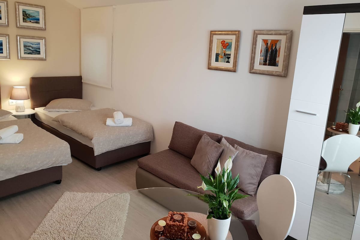 A hotel room with two beds, a sofa, a small table with a plant, and artwork on the walls.