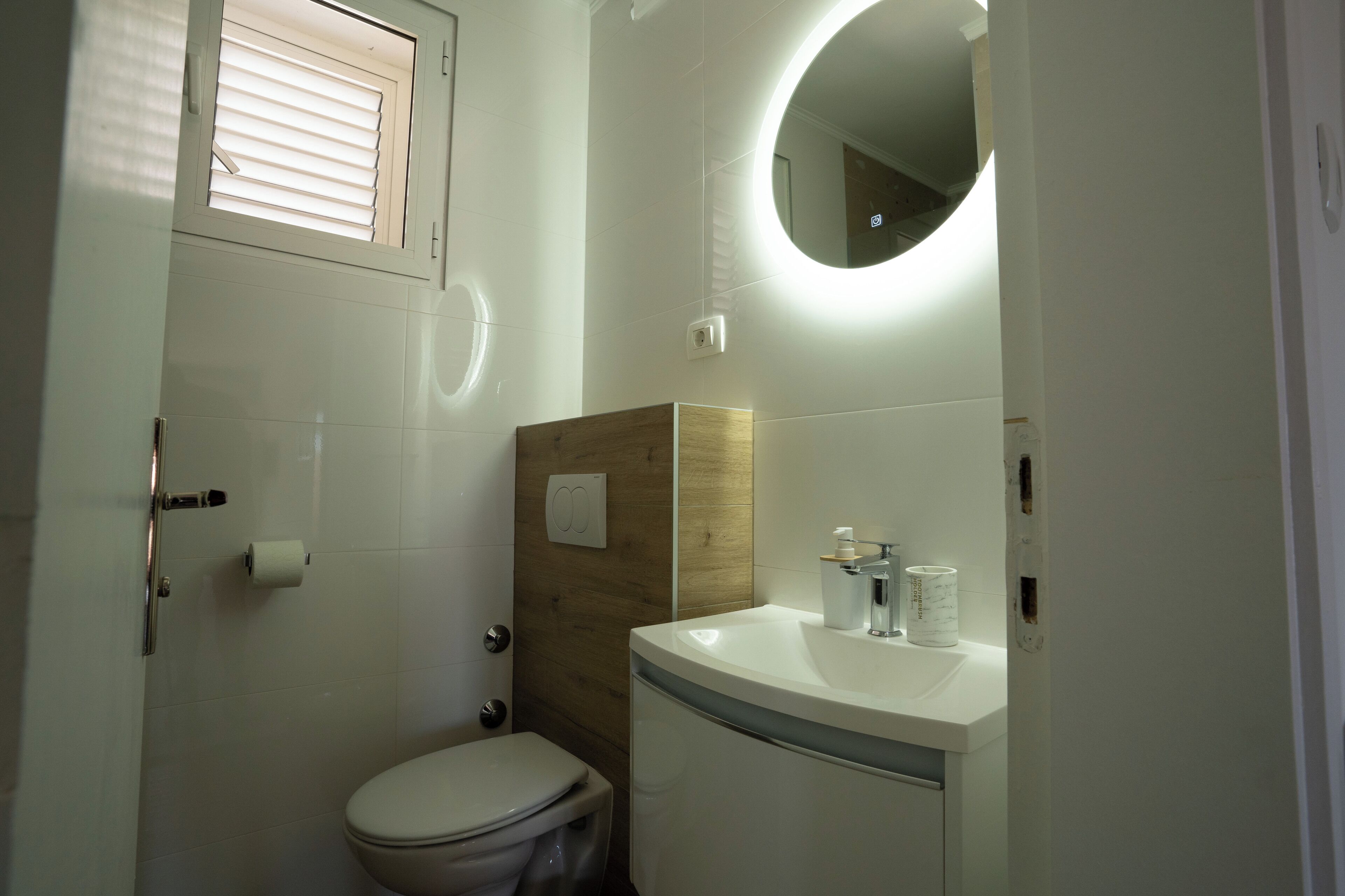 A bathroom with a toilet, sink, mirror, and window with blinds.