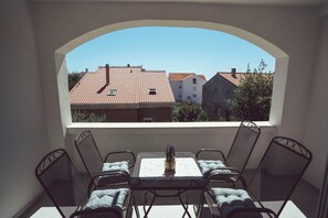 A balcony with a table and chairs, offering a view of red-tiled roofs and neighboring buildings. - Apartments & Rooms Petra (Zadar)